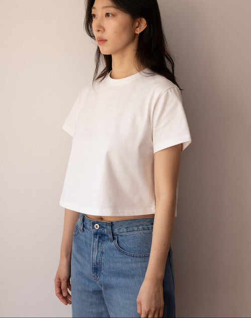 Woman wearing a white t-shirt and blue jeans against a plain wall