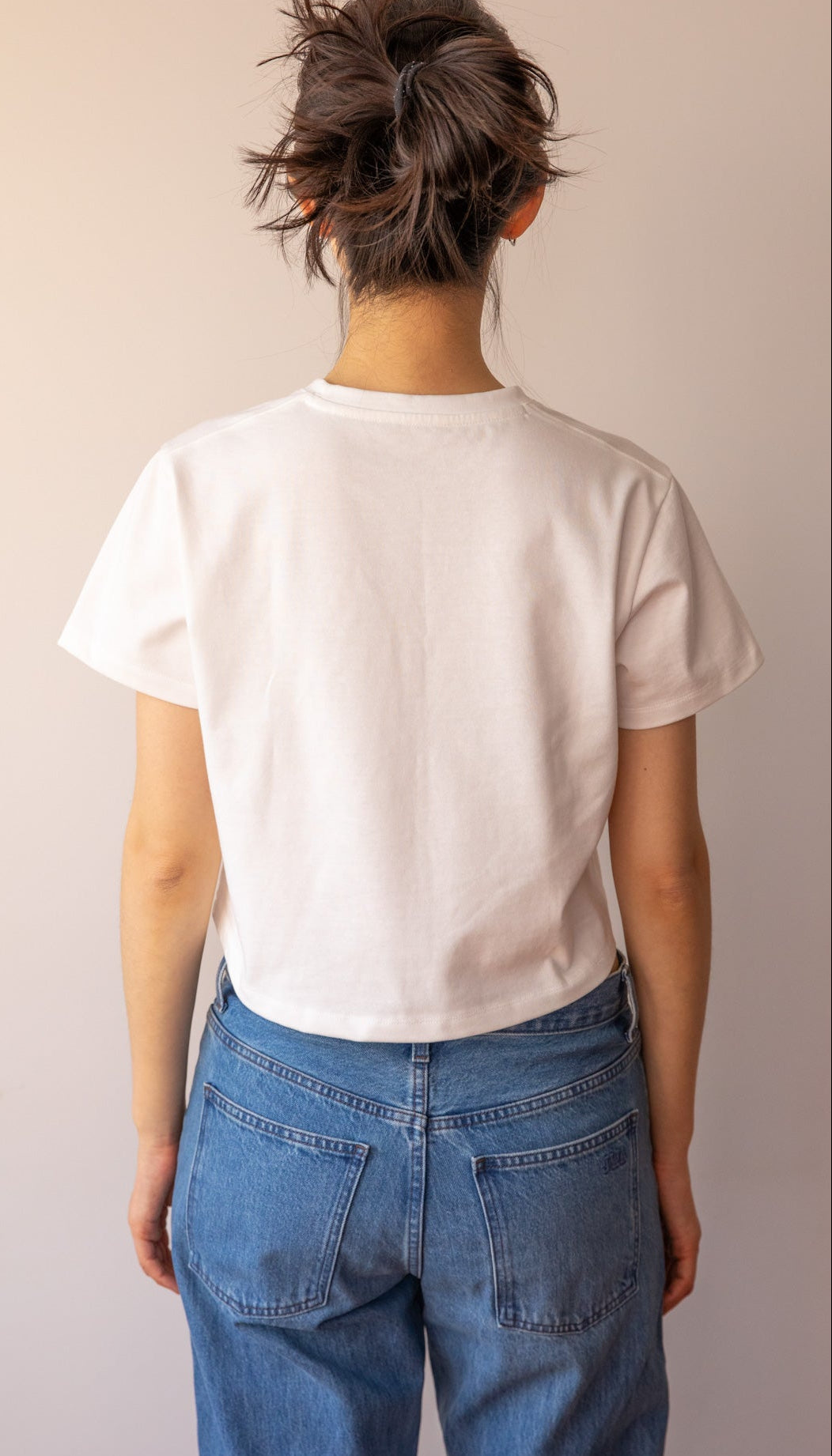 Person wearing a white t-shirt and blue jeans from behind on a plain background