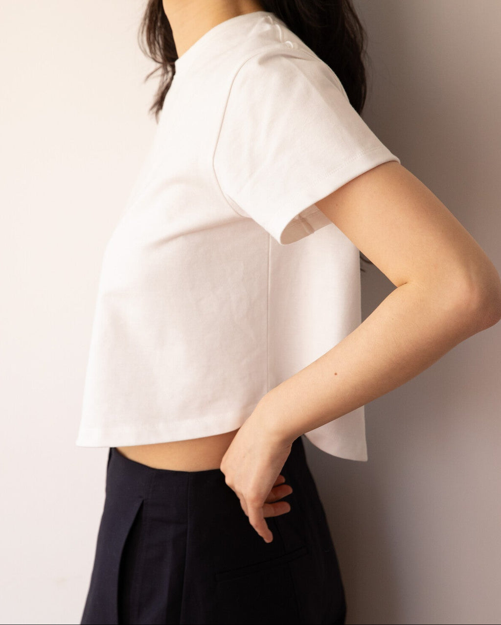 Person wearing a white cropped shirt and dark pants against a plain background