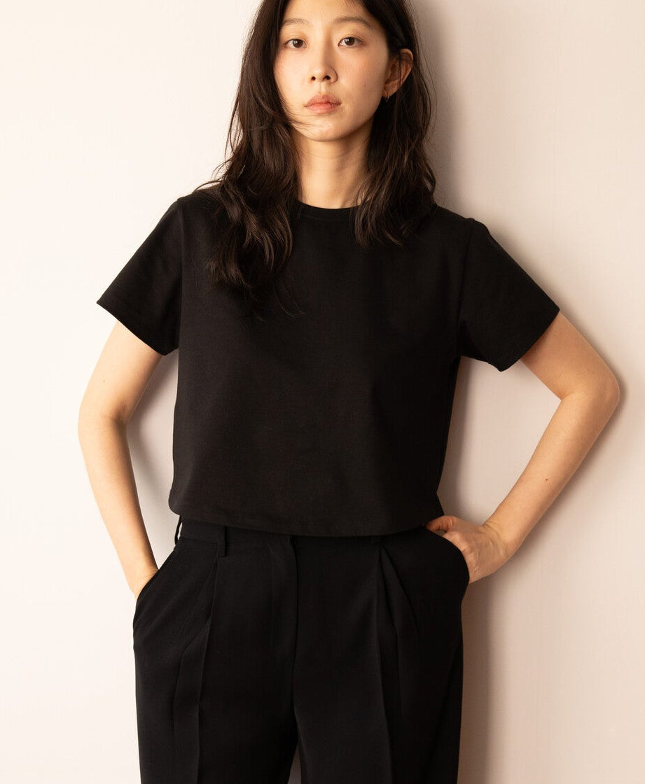 Person wearing a black outfit standing against a plain wall.