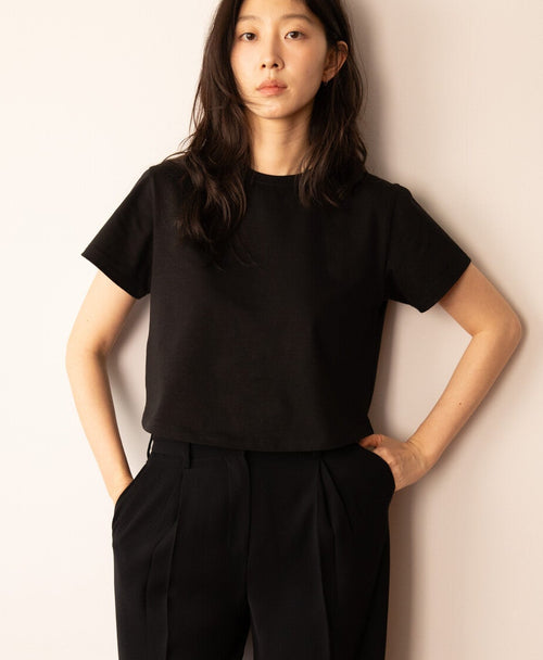 Person wearing a black outfit standing against a plain wall.